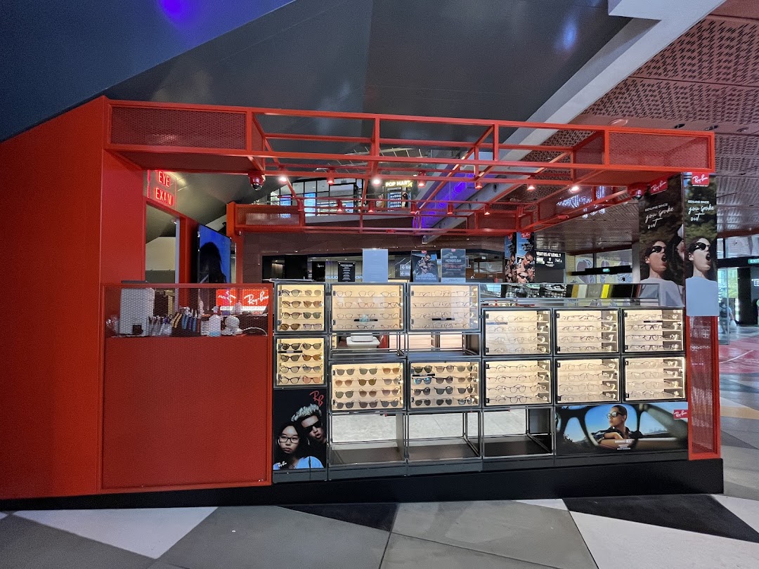 A vibrant red Ray-Ban kiosk showcasing a wide array of stylish eyeglasses and sunglasses in display cases.