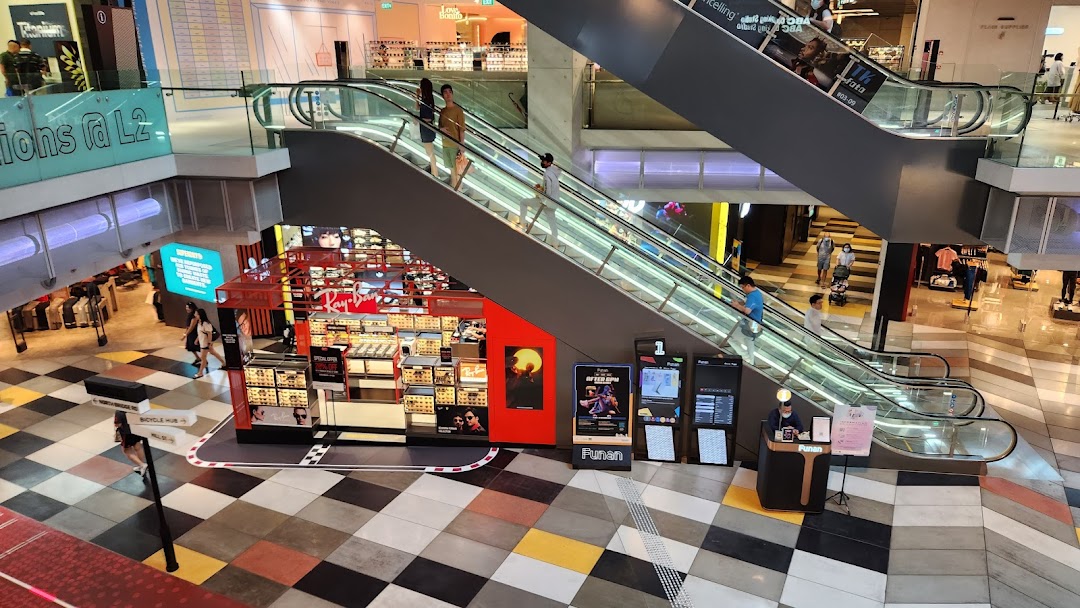 An aerial view of the Ray-Ban kiosk in Funan mall, located near escalators on a checkered floor.