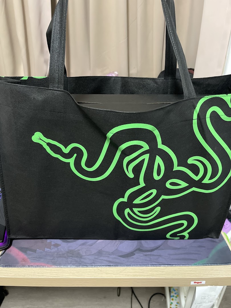 A black Razer tote bag with the iconic green triple-headed snake logo, sitting on a desk.