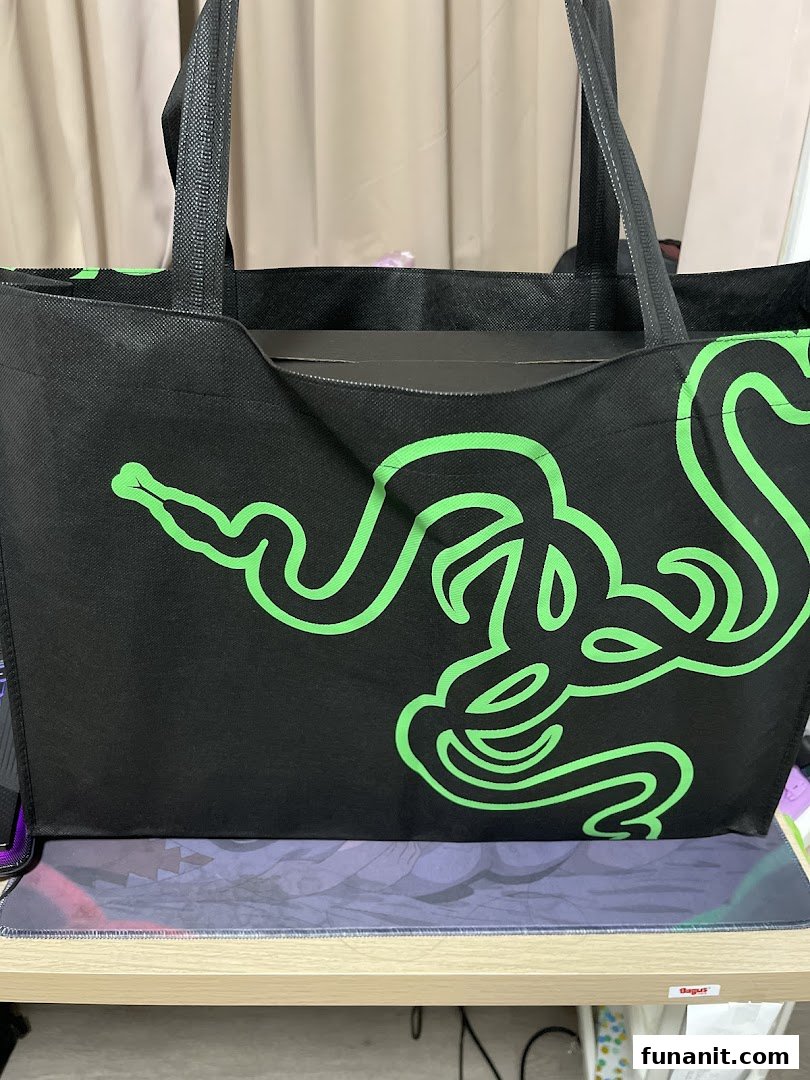 A black Razer tote bag with the iconic green triple-headed snake logo, sitting on a desk.