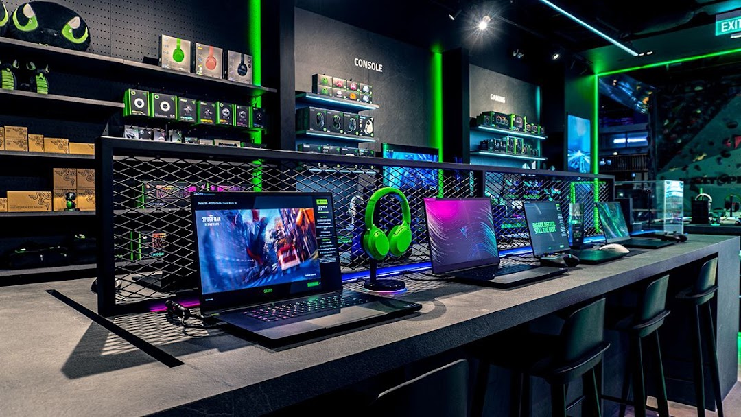 Interior view of RazerStore Funan showcasing gaming laptops, peripherals, and accessories in a sleek, dark setting with green lighting.