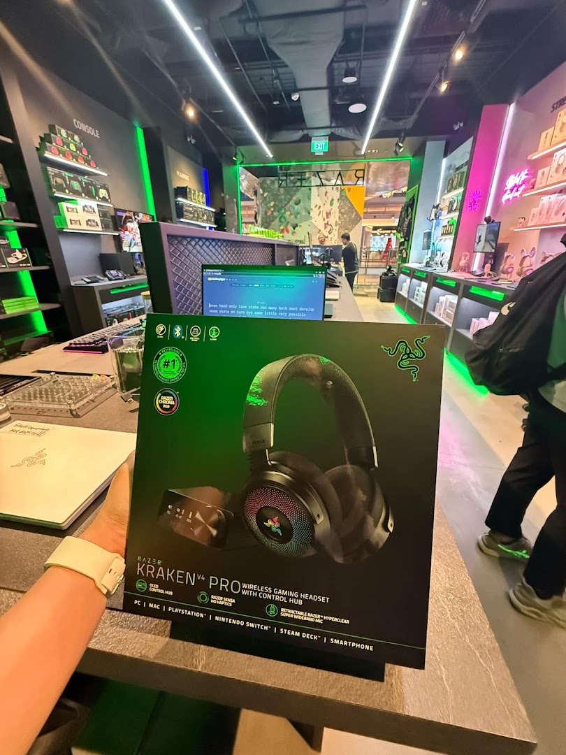 A customer holds a Razer Kraken V4 Pro headset box inside the vibrant RazerStore, showcasing gaming gear.