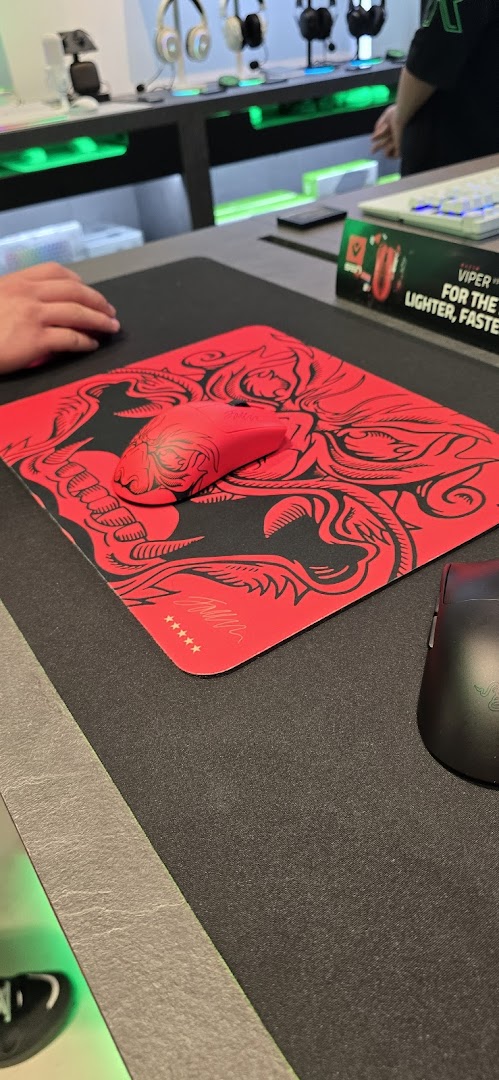 A red Razer gaming mouse on a matching mousepad, with other peripherals displayed in a tech store.