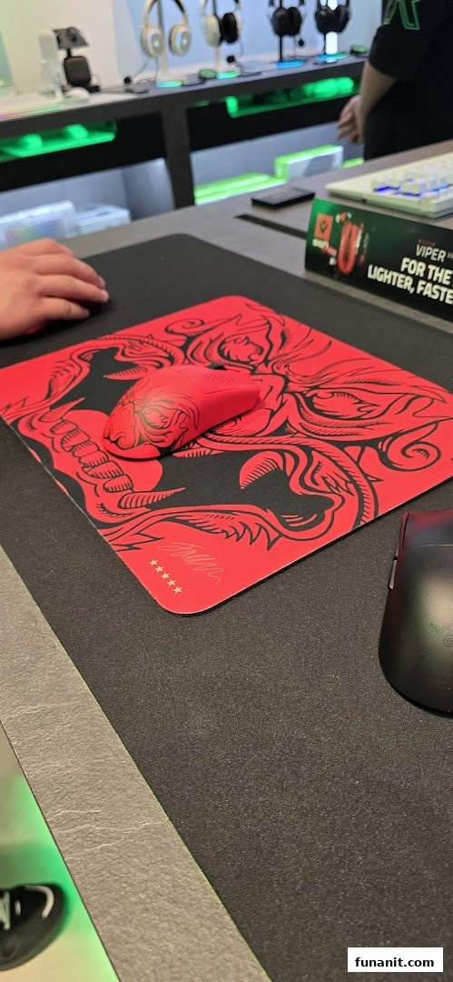 A red Razer gaming mouse on a matching mousepad, with other peripherals displayed in a tech store.