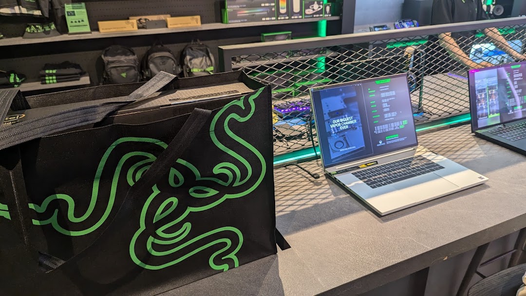 Interior view of RazerStore Funan showcasing gaming laptops, merchandise, and a branded tote bag.