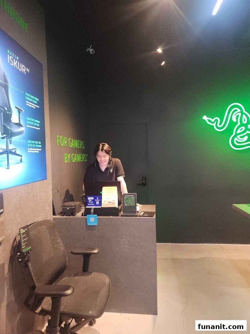 An interior view of RazerStore Funan, featuring a staff member, a gaming chair display, and the brand's iconic green neon logo.