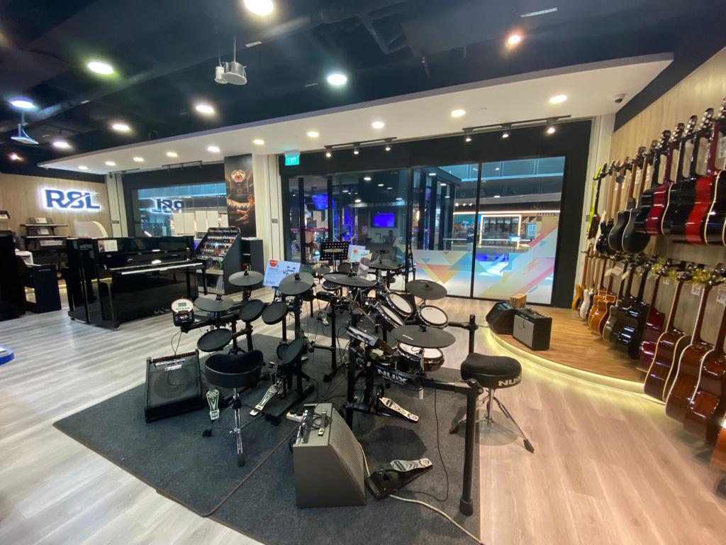 An interior view of a music instrument shop featuring pianos, electronic drums, and a wall of guitars.