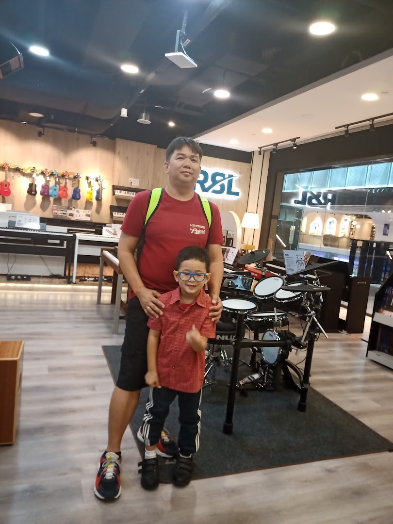 A man and a child pose in a music instrument shop featuring drums, keyboards, and ukuleles.