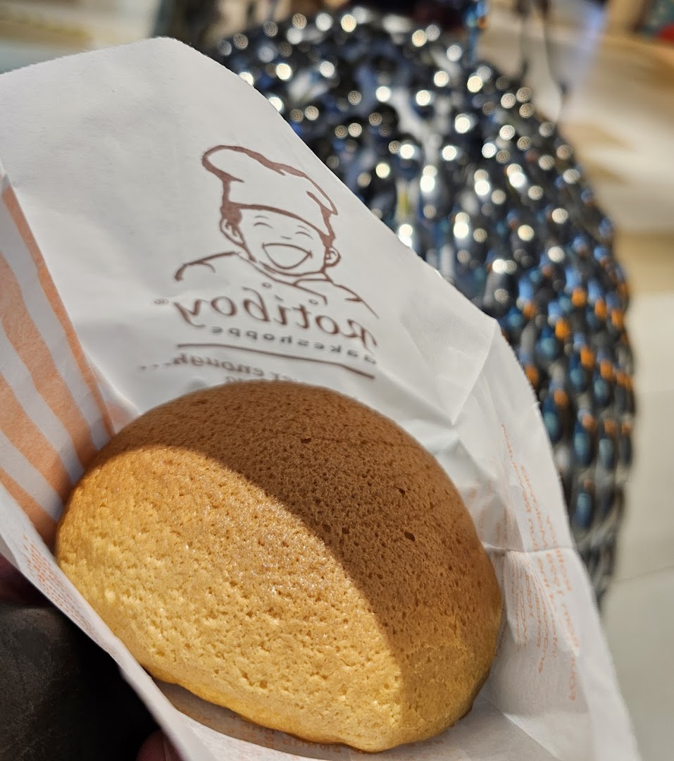 A freshly baked Rotiboy bun held in its branded paper bag, showcasing its golden-brown crust.