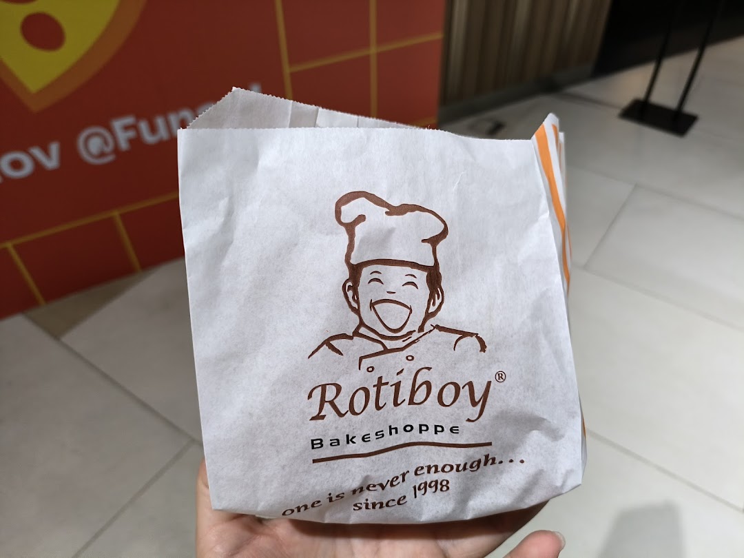 A hand holds a Rotiboy Bakeshoppe paper bag featuring its iconic logo and slogan.