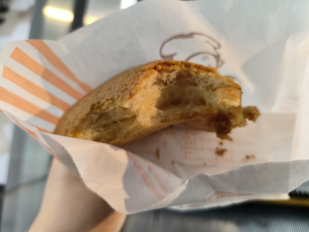 A partially eaten Rotiboy bun, revealing its soft interior, held in its signature striped paper bag.