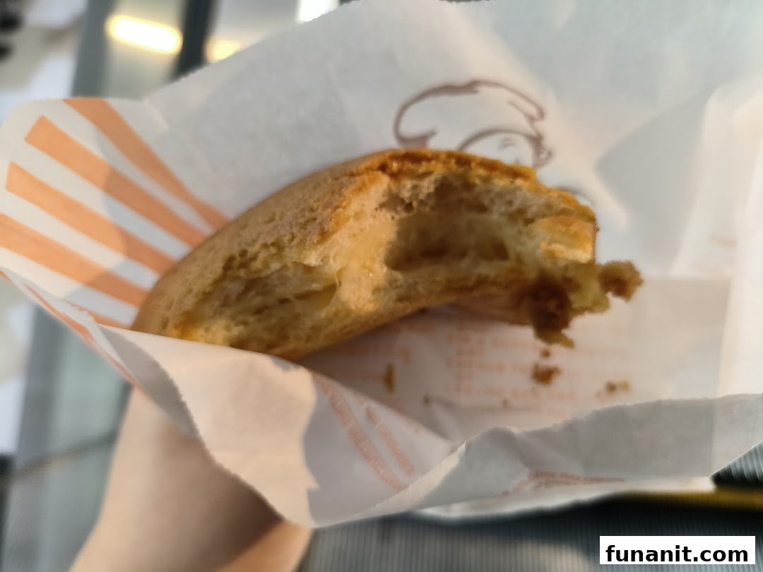 A partially eaten Rotiboy bun, revealing its soft interior, held in its signature striped paper bag.