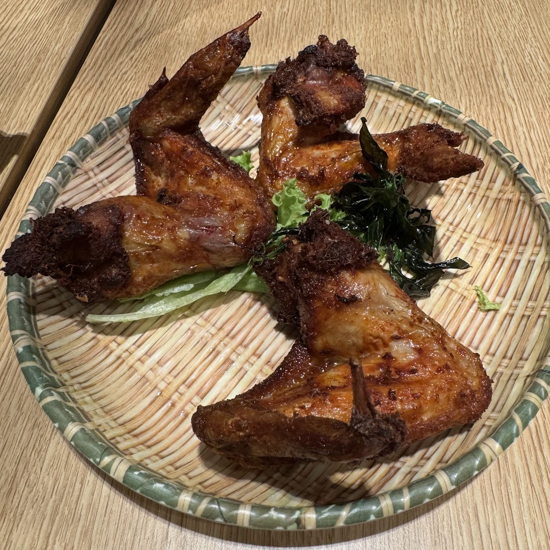 A close-up of crispy fried chicken wings served on a traditional woven platter with greens.