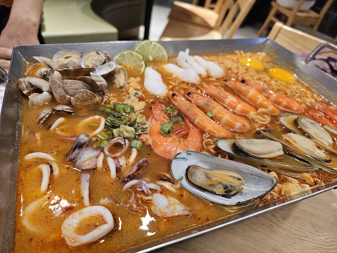 A large pan of vibrant tom yum seafood soup with noodles, prawns, mussels, clams, and squid.