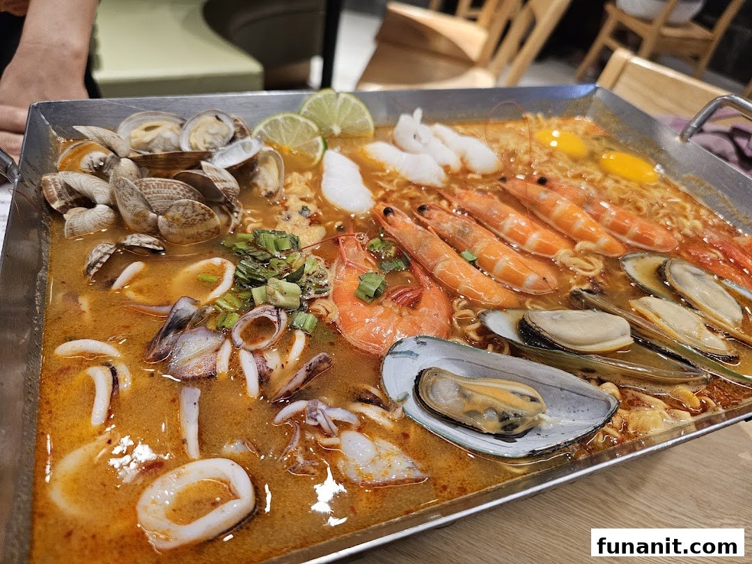 A large pan of vibrant tom yum seafood soup with noodles, prawns, mussels, clams, and squid.