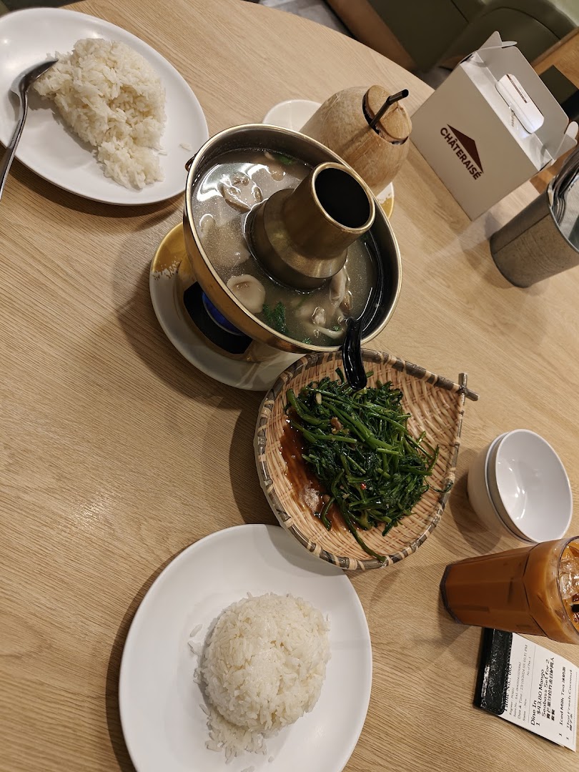 A table laden with delicious Thai dishes, including a hotpot, stir-fried greens, rice, and refreshing drinks.