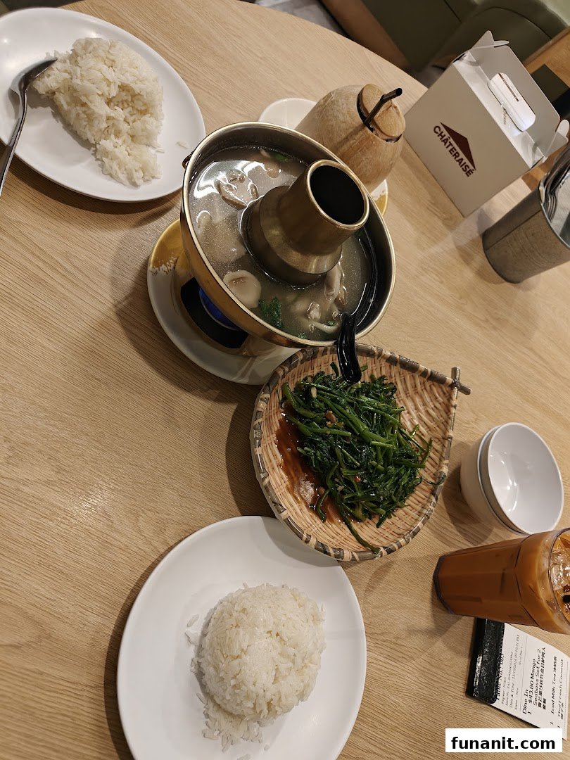 A table laden with delicious Thai dishes, including a hotpot, stir-fried greens, rice, and refreshing drinks.