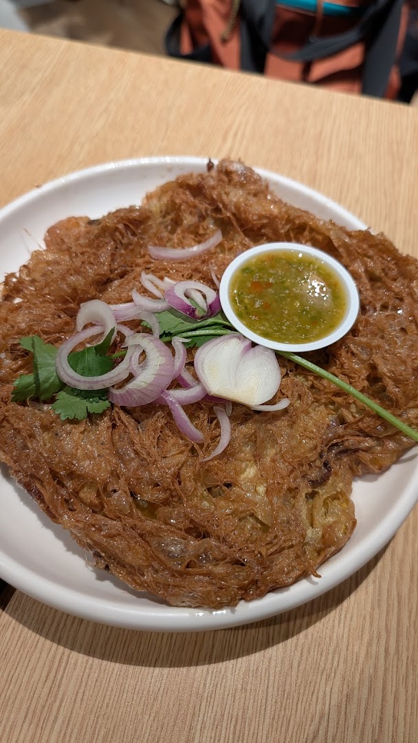 A crispy Thai omelette dish with fresh herbs and a side of spicy dipping sauce.