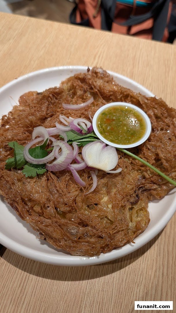 A crispy Thai omelette dish with fresh herbs and a side of spicy dipping sauce.