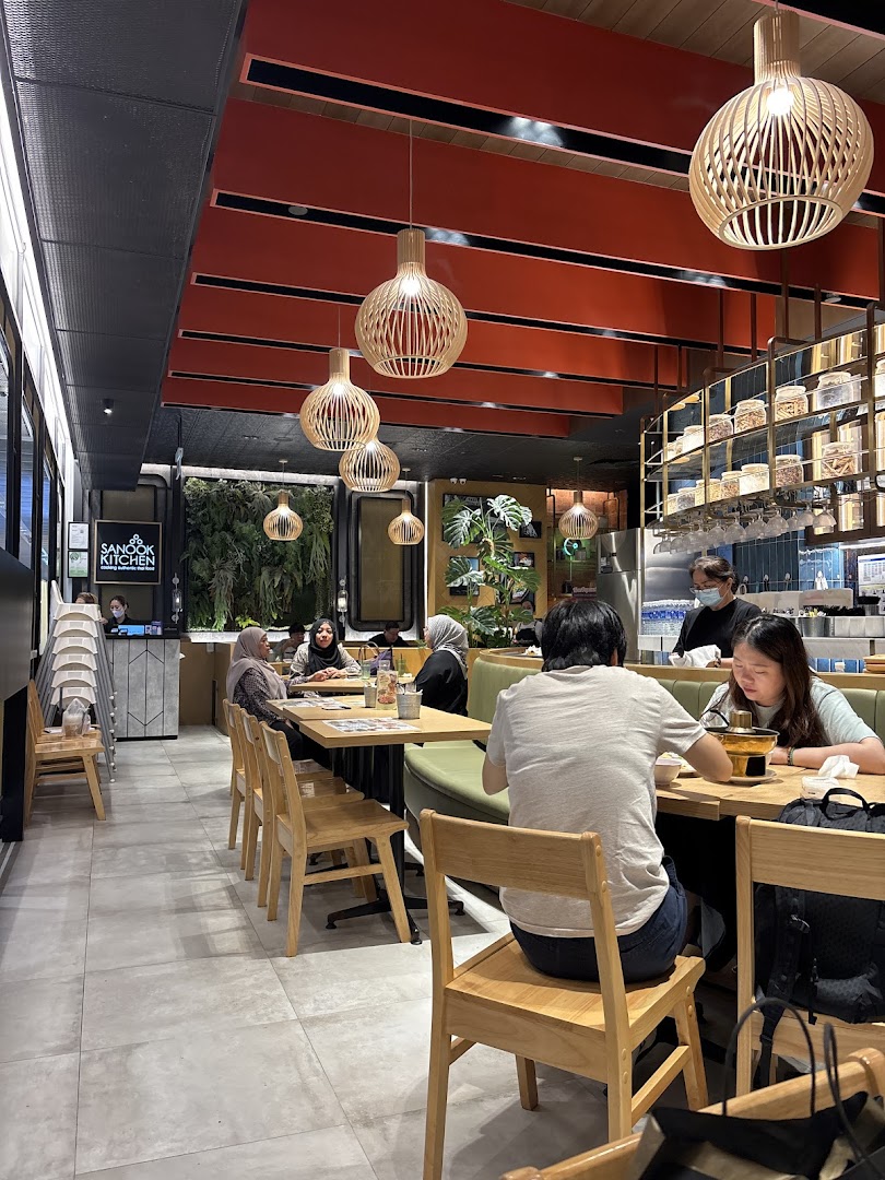 Diners enjoy a meal in the vibrant, modern interior of Sanook Kitchen, featuring unique lighting and lush greenery.