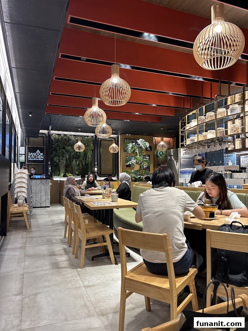 Diners enjoy a meal in the vibrant, modern interior of Sanook Kitchen, featuring unique lighting and lush greenery.