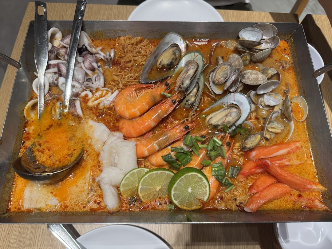 A large pan of vibrant tom yum seafood with prawns, mussels, clams, squid, and noodles.