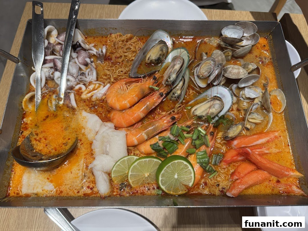 A large pan of vibrant tom yum seafood with prawns, mussels, clams, squid, and noodles.