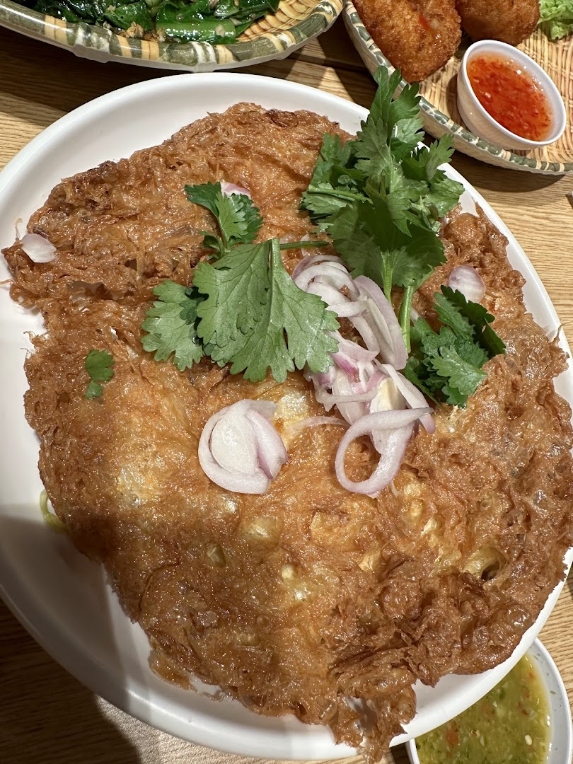 A close-up of a crispy Thai omelette garnished with fresh cilantro and sliced red onions.