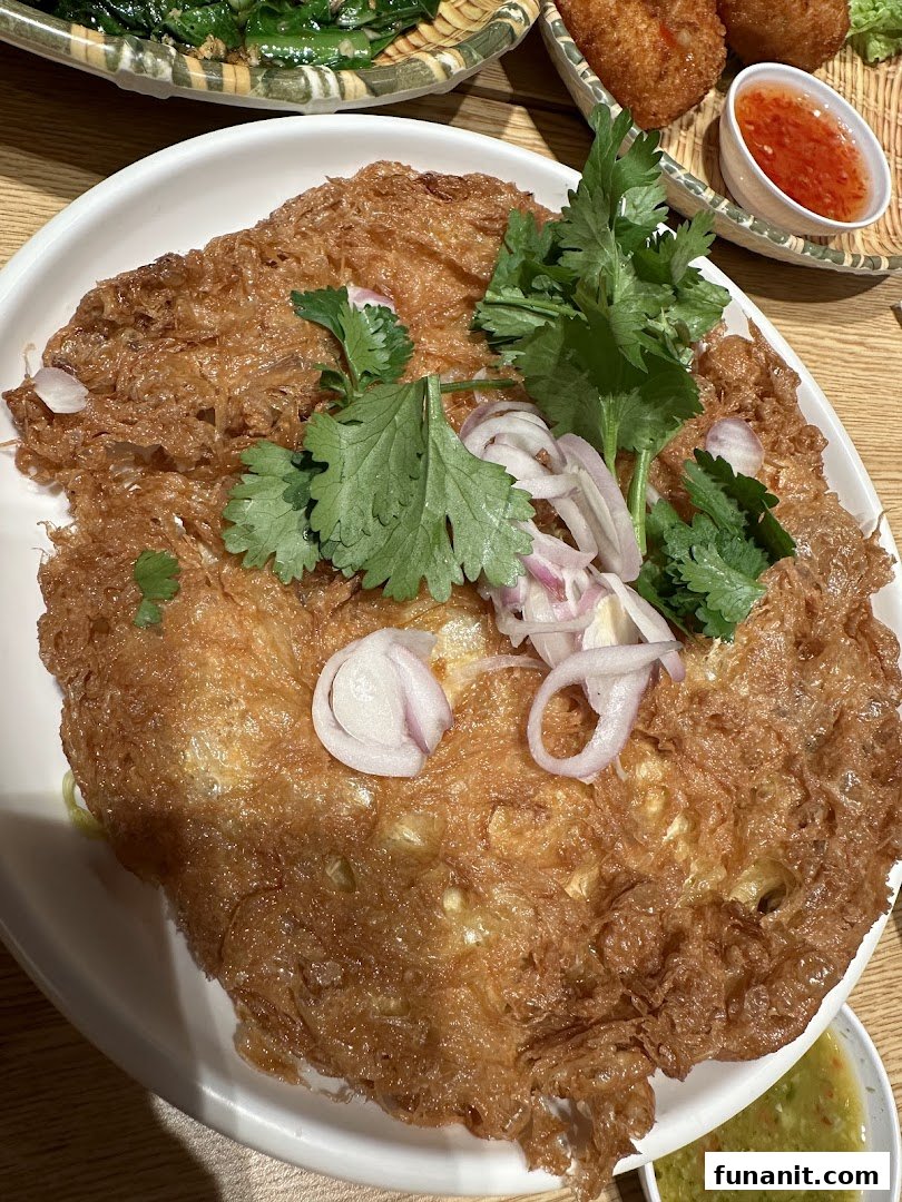 A close-up of a crispy Thai omelette garnished with fresh cilantro and sliced red onions.