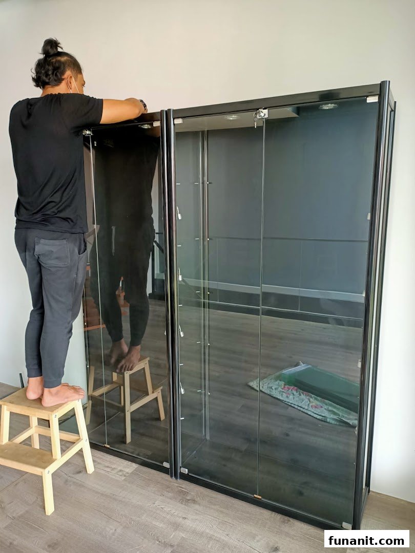 A person assembling or adjusting a black-framed glass display cabinet for toys or collectibles.