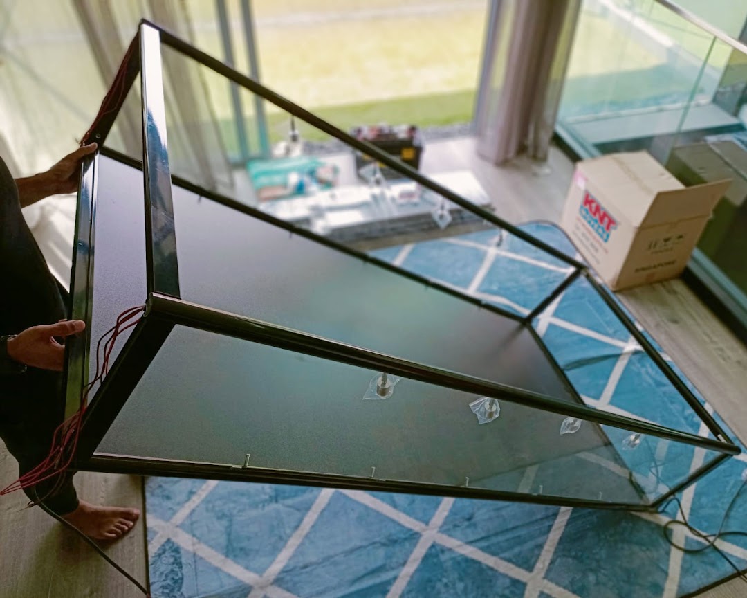 A person assembling or moving a black-framed glass display case on a patterned rug.
