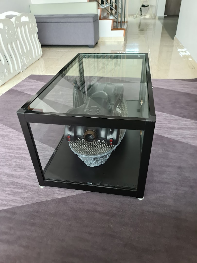A glass display coffee table showcasing a detailed Batmobile model in an interior setting.