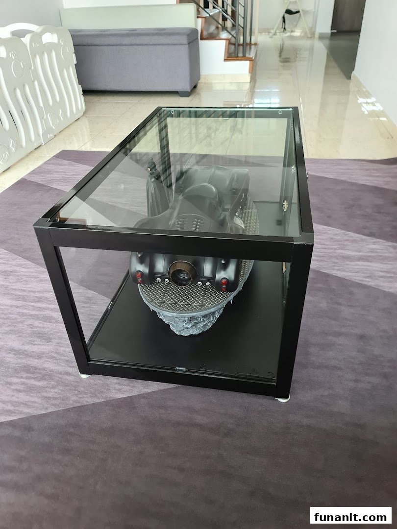 A glass display coffee table showcasing a detailed Batmobile model in an interior setting.
