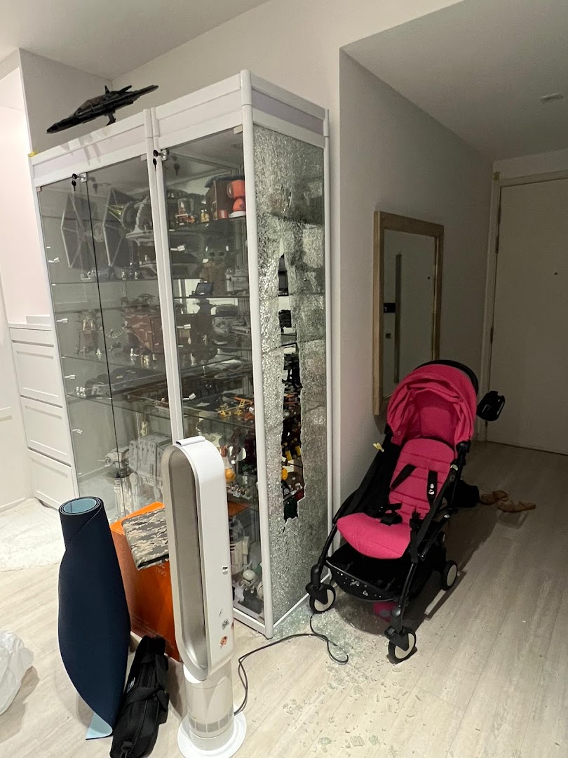 A display cabinet filled with toys and collectibles, featuring a broken glass panel and scattered shards.