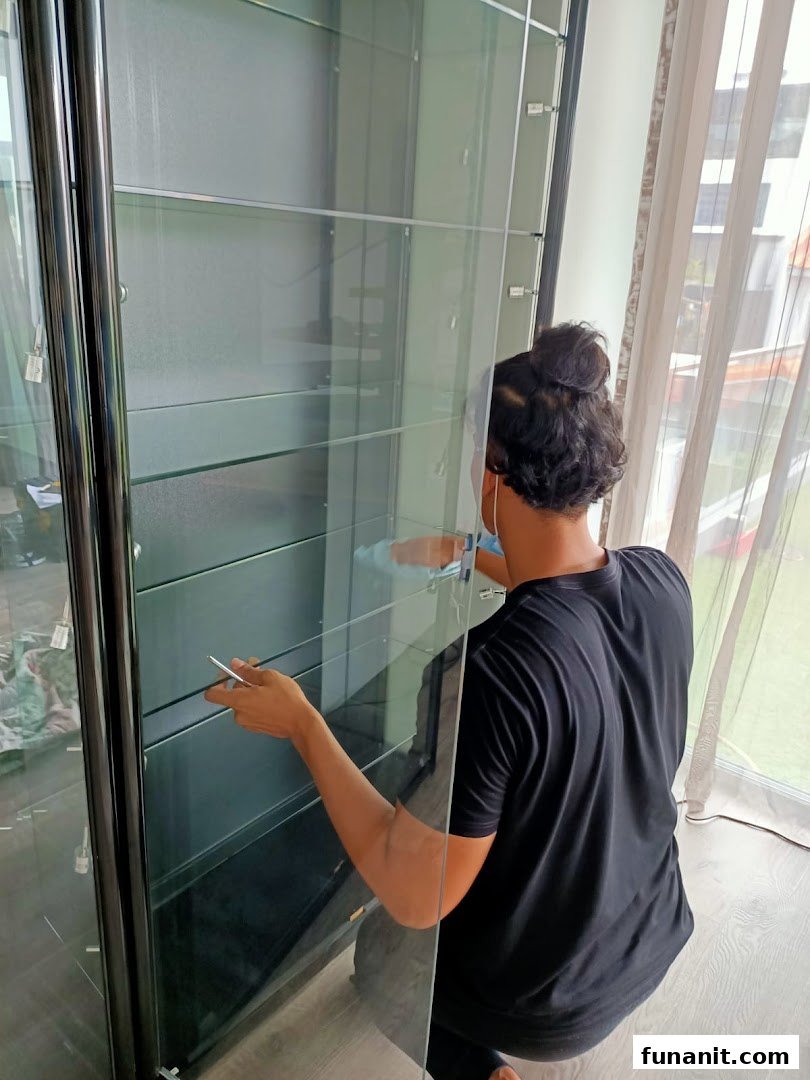 A person is assembling or cleaning a large, multi-shelf glass display cabinet.