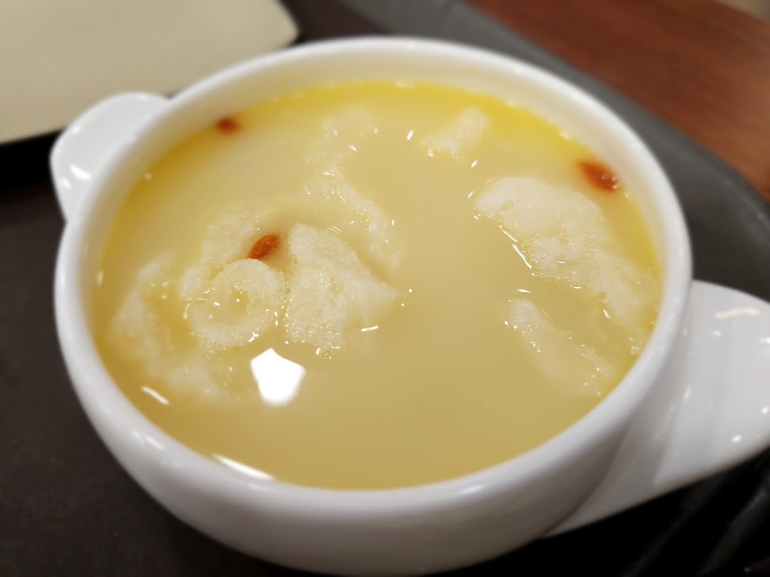 A close-up of a creamy yellow dessert or soup with goji berries in a white bowl.
