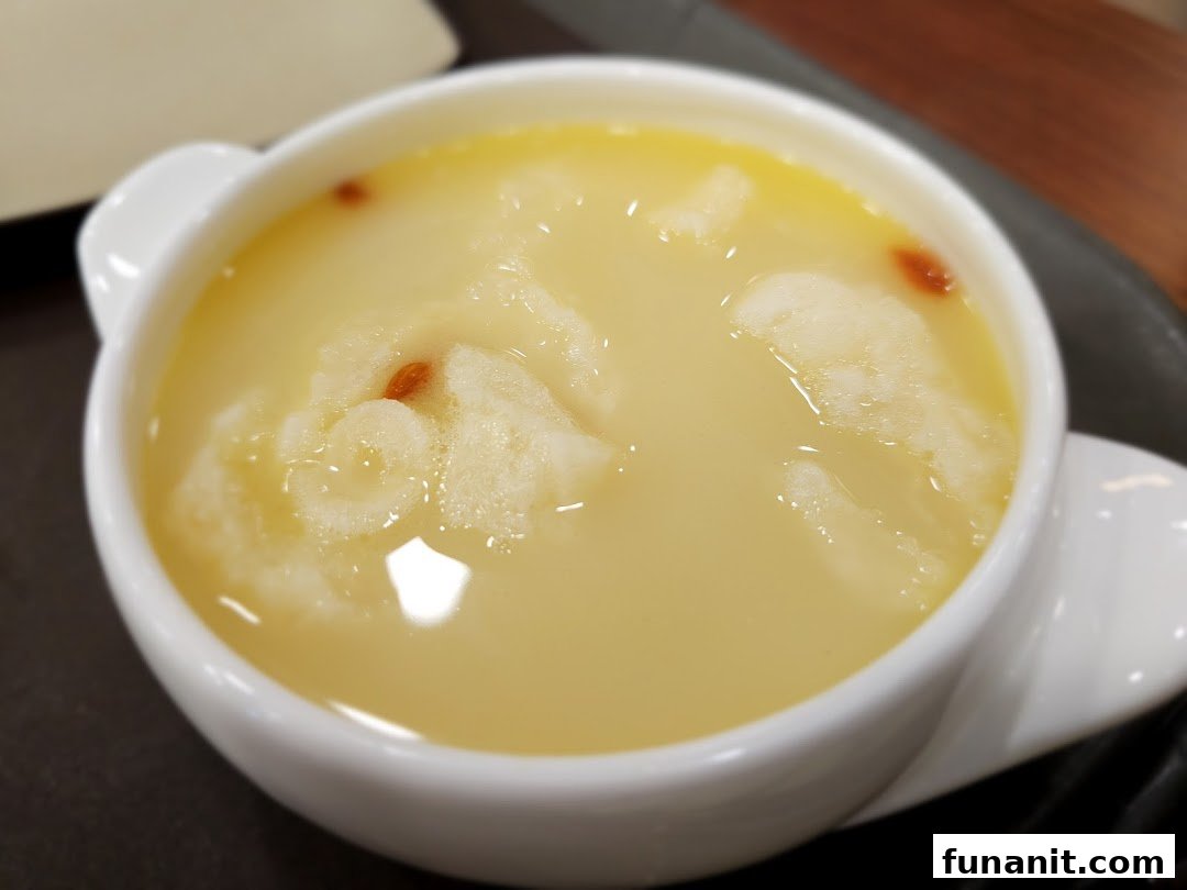 A close-up of a creamy yellow dessert or soup with goji berries in a white bowl.