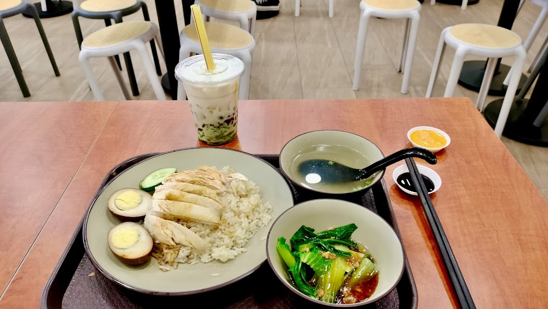 A delicious plate of chicken rice with side dishes, soup, and a bubble tea drink on a table.
