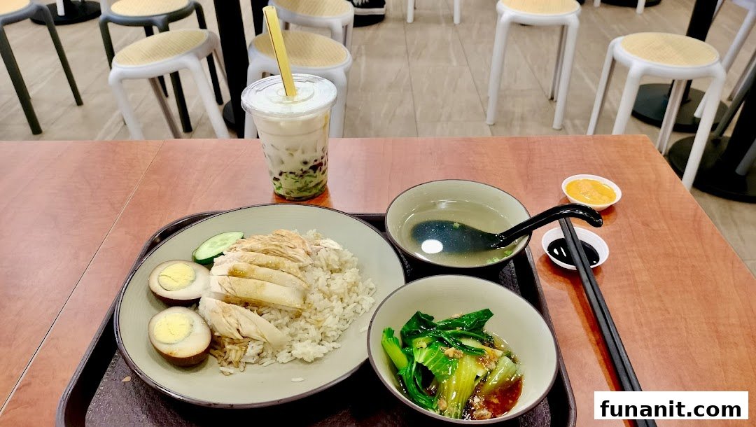 A delicious plate of chicken rice with side dishes, soup, and a bubble tea drink on a table.