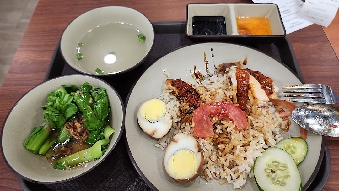 A delicious plate of roasted chicken rice with sides of vegetables, soup, and dipping sauces.
