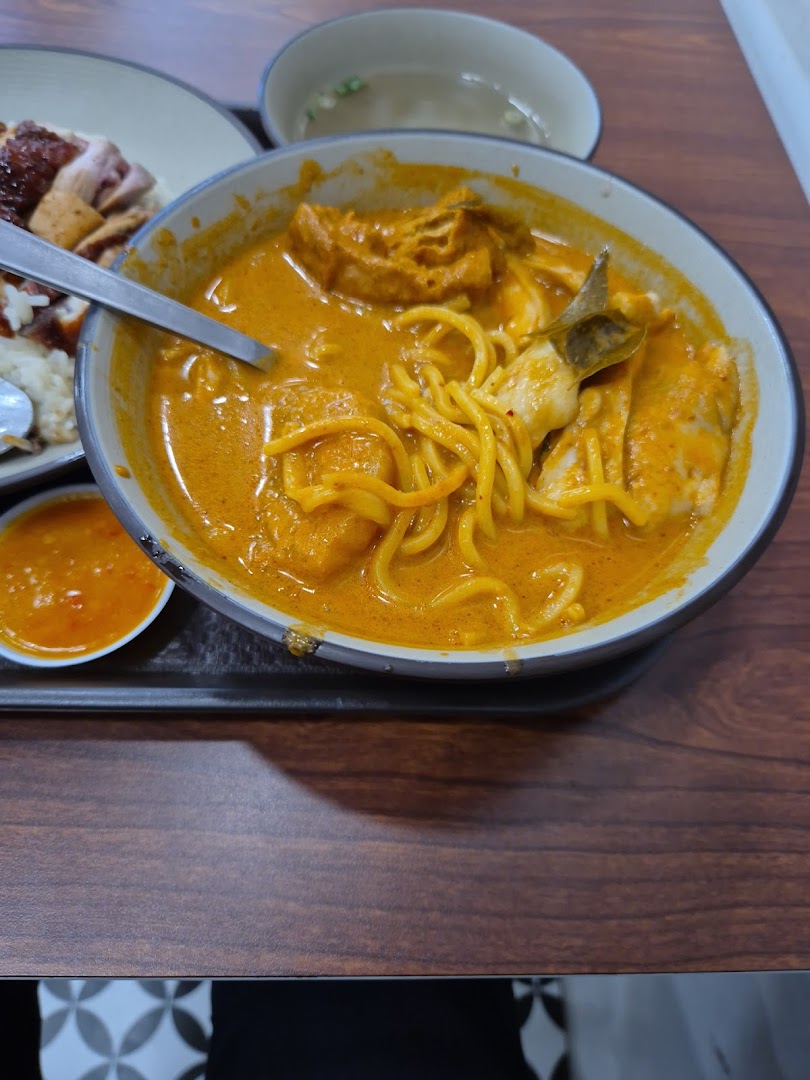 A vibrant bowl of curry noodles with a side of roasted meat and rice.