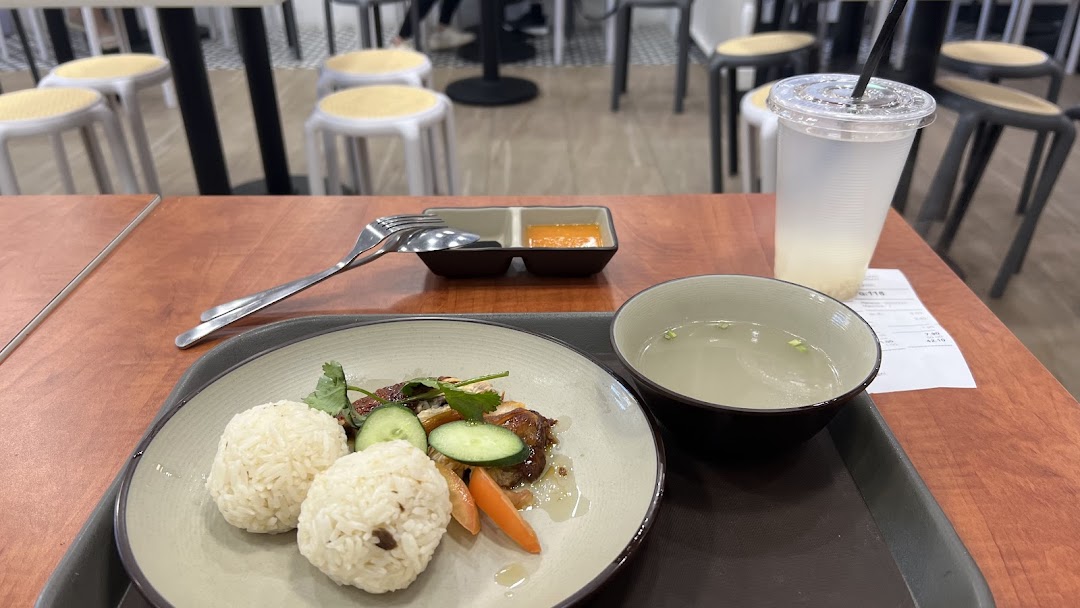 A delicious plate of chicken rice with soup and a drink served on a wooden table.