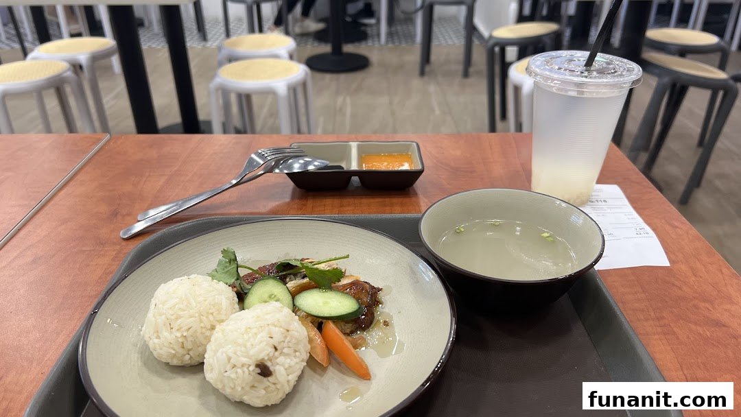A delicious plate of chicken rice with soup and a drink served on a wooden table.