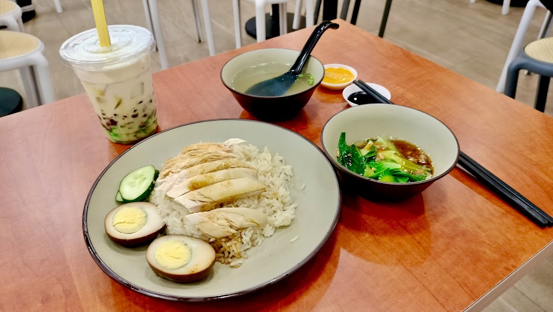 A delicious Hainanese chicken rice set with soup, vegetables, braised eggs, and a bubble tea drink.