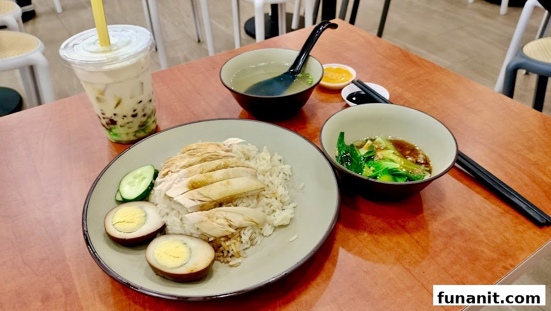A delicious Hainanese chicken rice set with soup, vegetables, braised eggs, and a bubble tea drink.