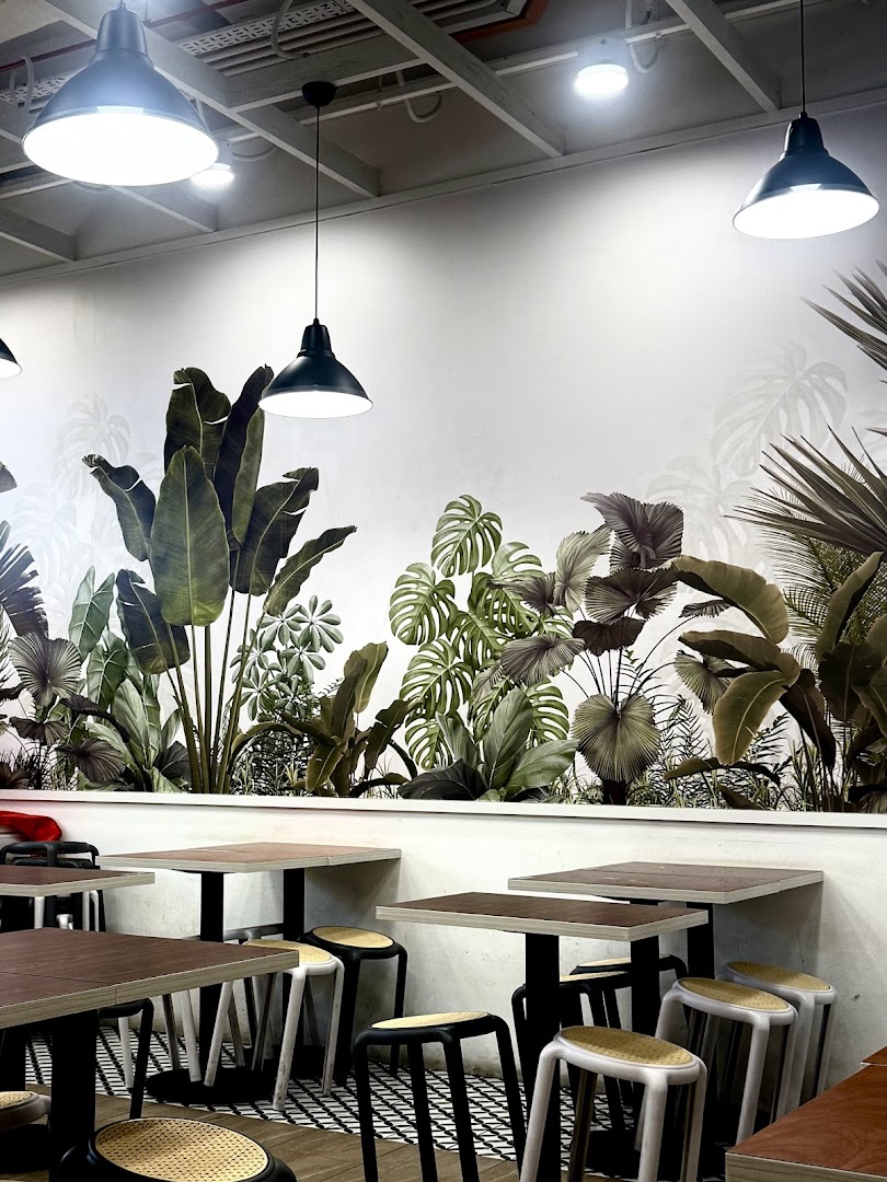 Interior dining area with tropical plant mural, tables, and stools under industrial pendant lights.
