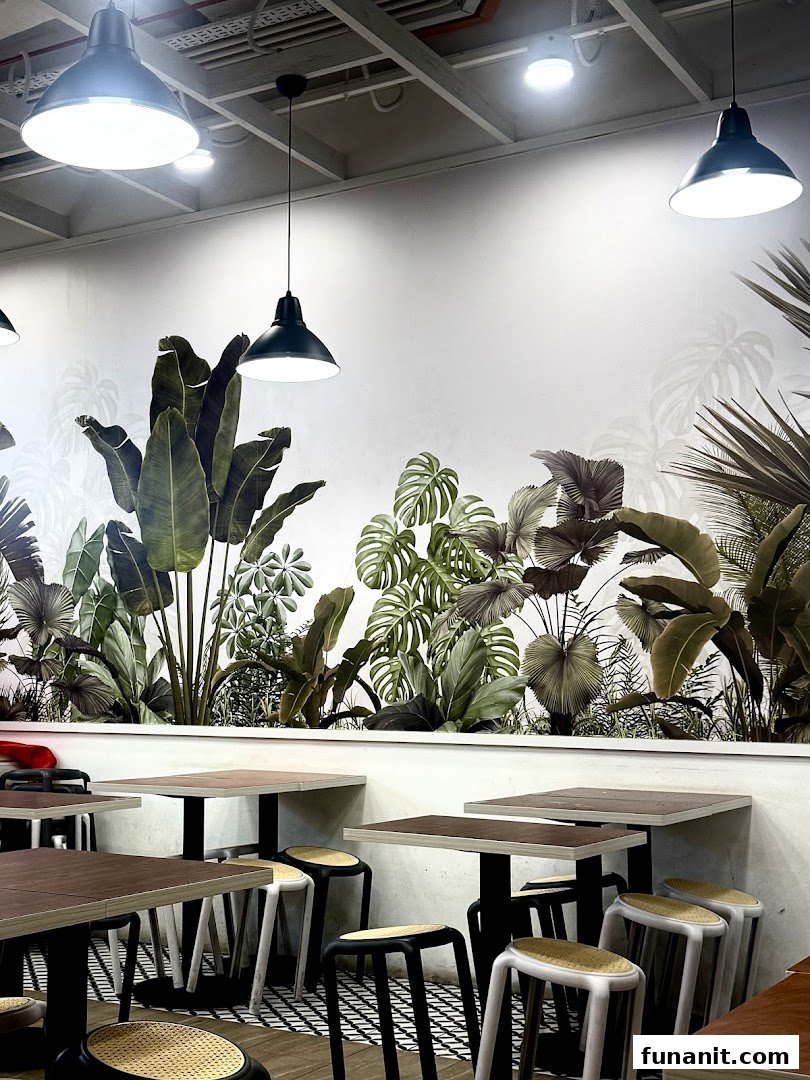 Interior dining area with tropical plant mural, tables, and stools under industrial pendant lights.