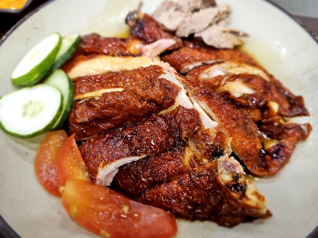 A close-up of Sing Swee Kee's roasted chicken with crispy skin, served with fresh cucumber and tomato.