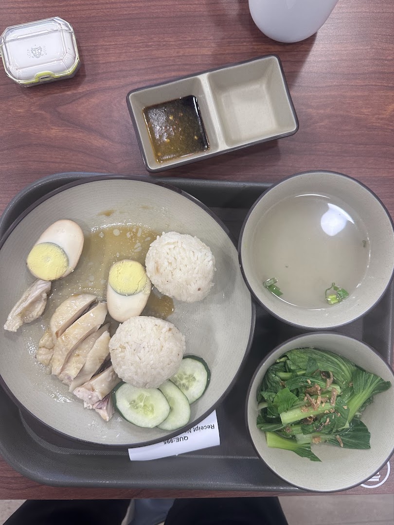 A delicious plate of Hainanese chicken rice with soup and vegetables on a wooden table.
