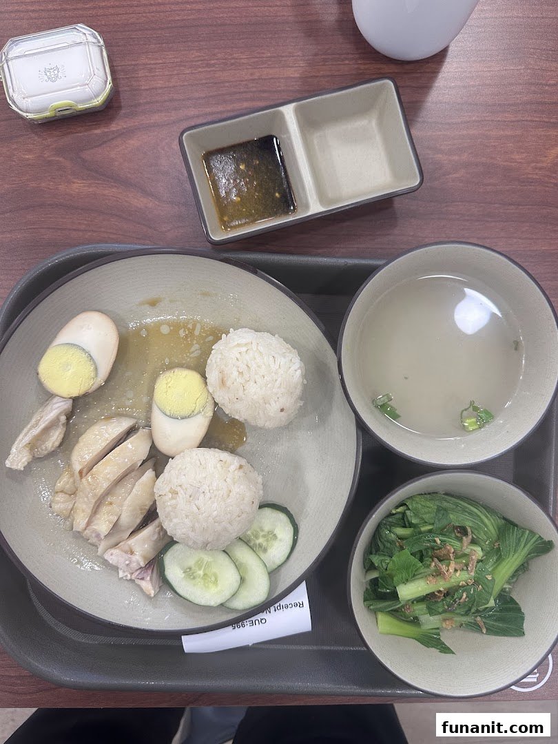 A delicious plate of Hainanese chicken rice with soup and vegetables on a wooden table.